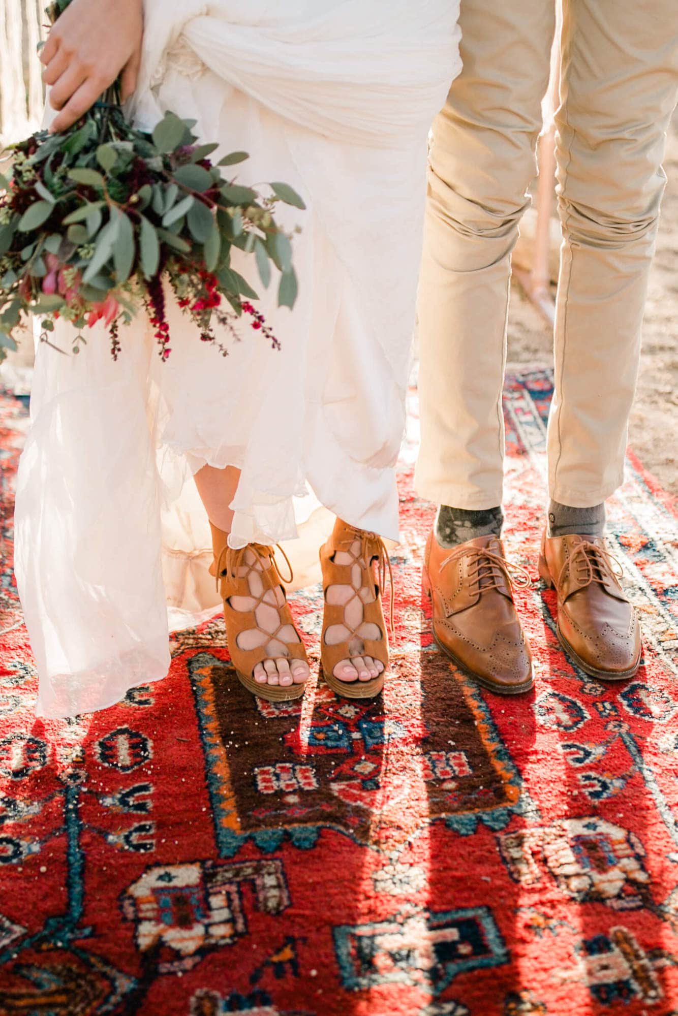 The bride and groom stand on a brightly patterned rug at their Joshua tree wedding.