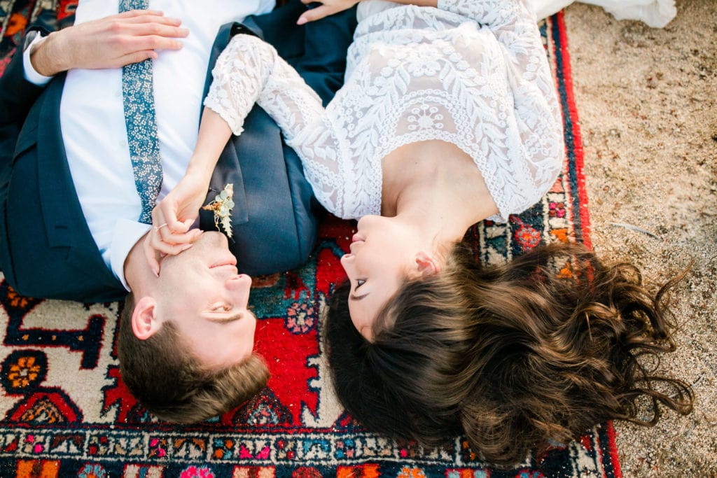 Bride and groom lay on a brightly patterned rug during their Joshua Tree wedding.