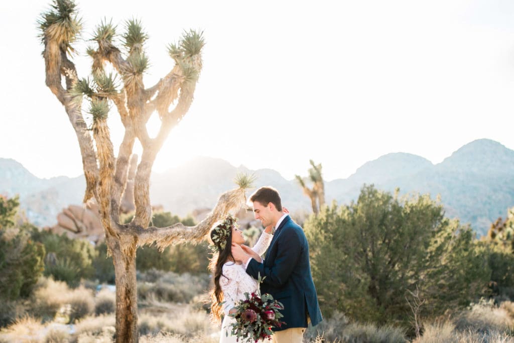 During their Joshua Tree wedding, the groom touches his brides face with the sun setting behind them.
