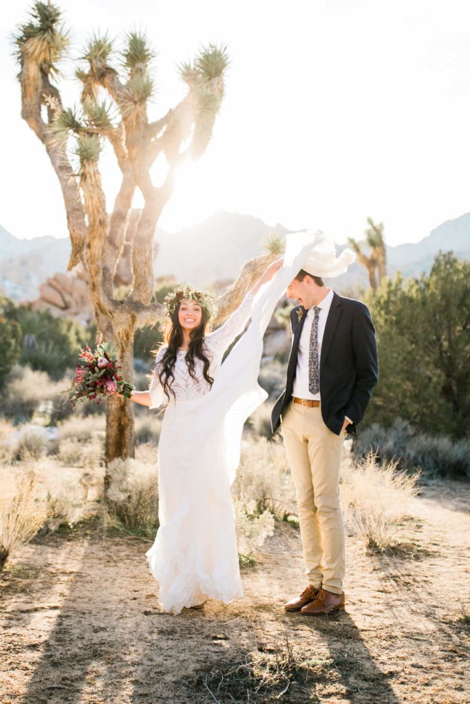 A smiling bride accidenally hits her groom in the face with her skirt during their joshua tree wedding.