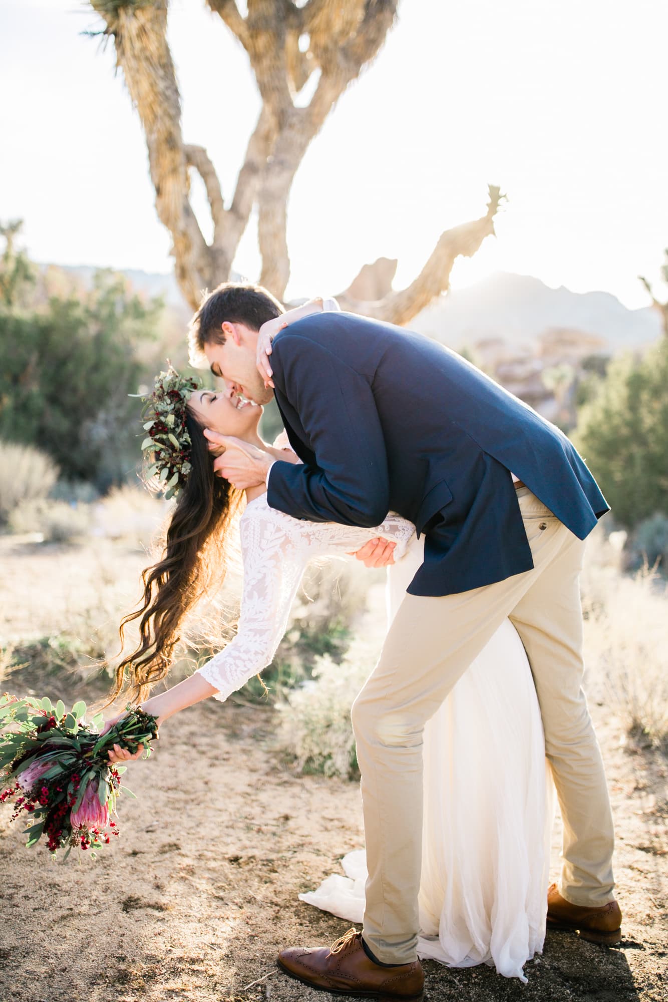 eloping couple celebrates with a first dance at sunset surrounded by joshua trees. the groom dips his bride as they smile.