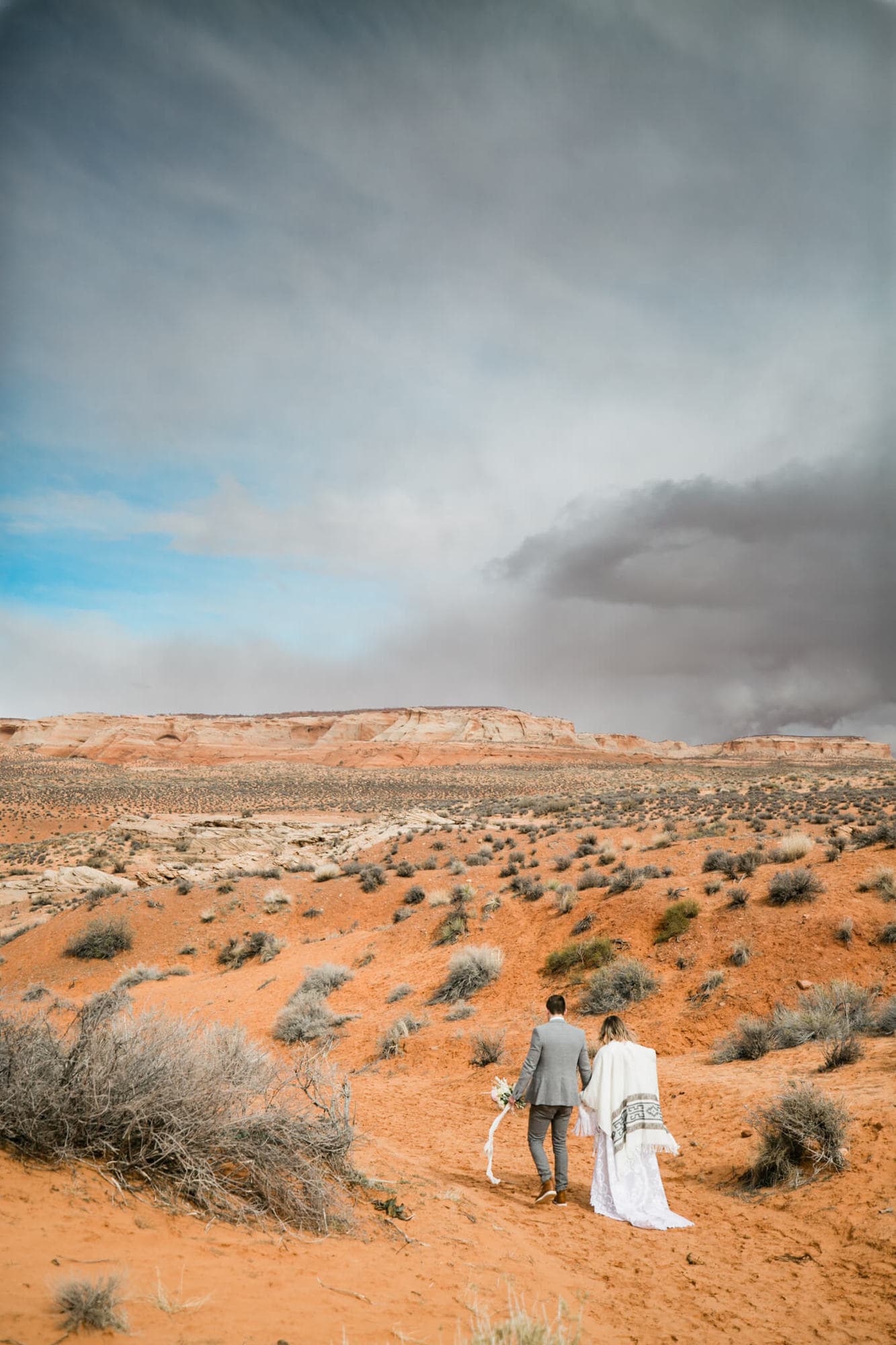 Adventurous couple walks hand in hand through the desert. A storm looms on the horizon.