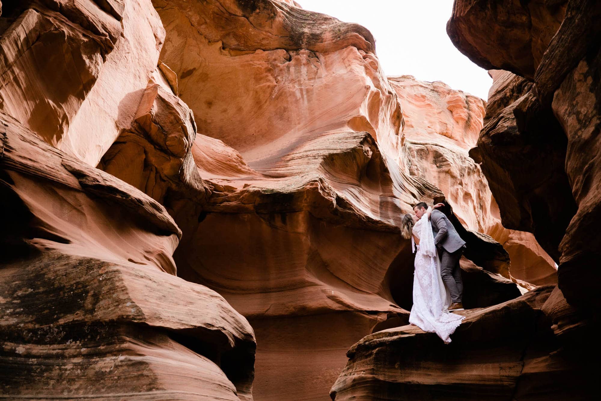 During their elopement in Arizona, the bride and groom share a kiss perched high on an outcropping of the slot canon.