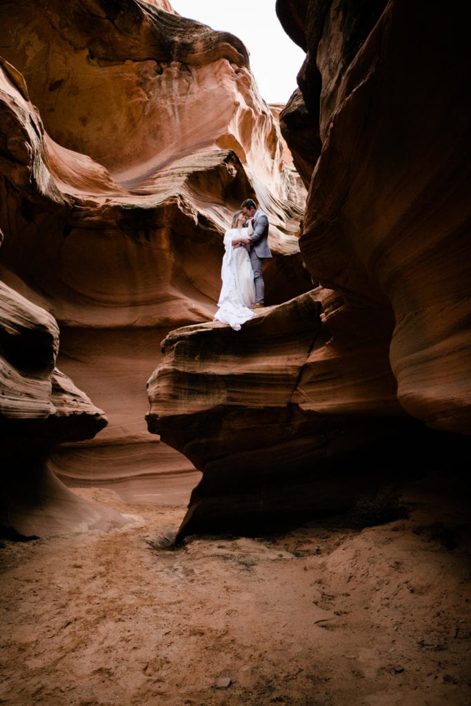 During their elopement in Arizona the bride leans back to kiss her groom, perched in a desert slot canyon. 