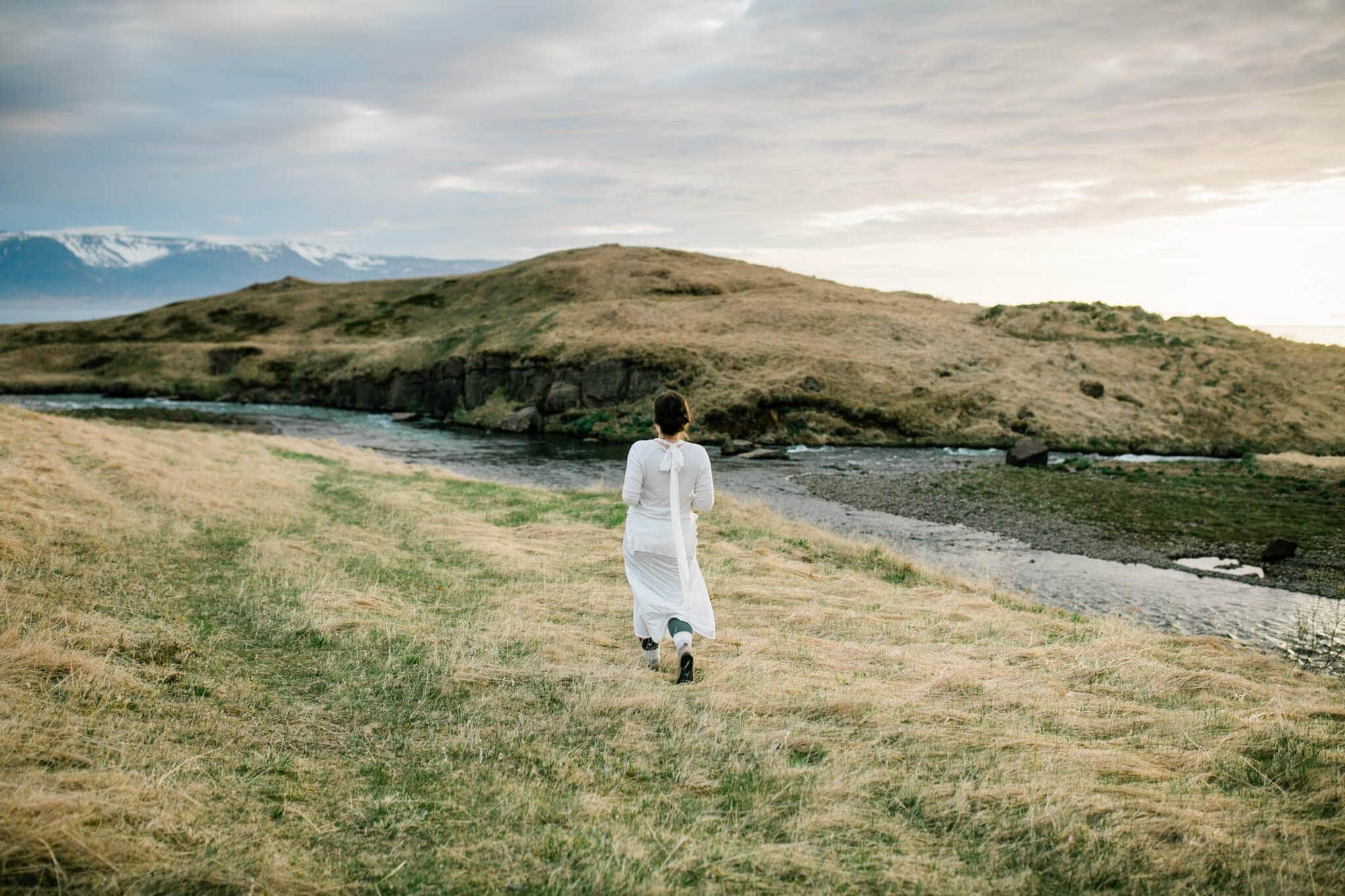 a bride walks towards a river in Iceland at sunset.