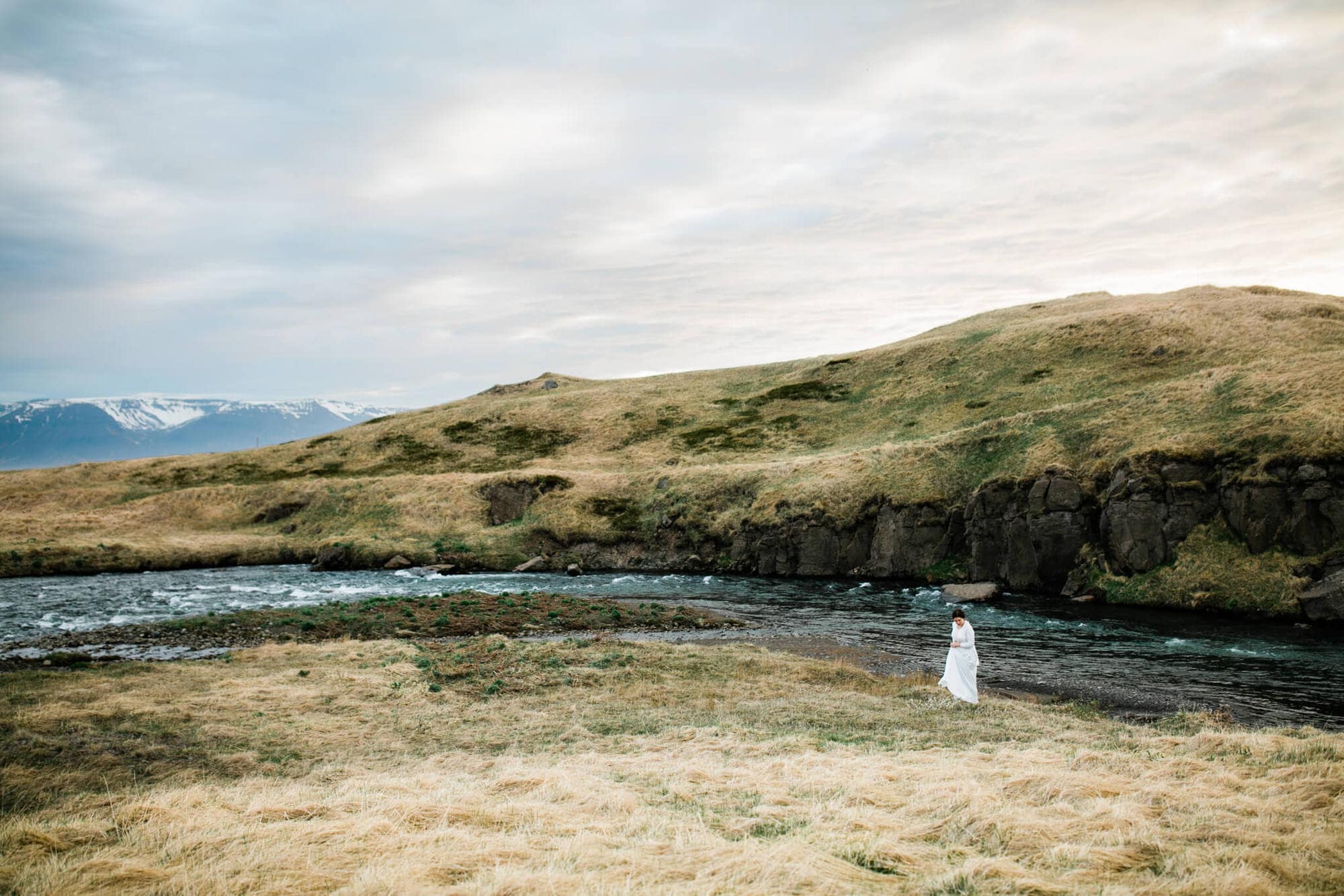 A bride walks beside a river at sunset during her Iceland Elopement.