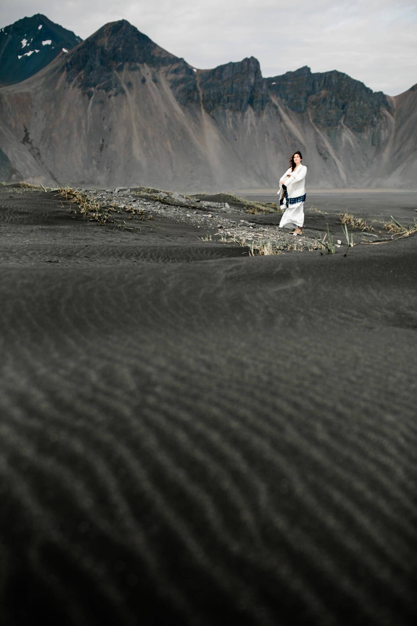 A bride stands among black sand dunes in Iceland.
