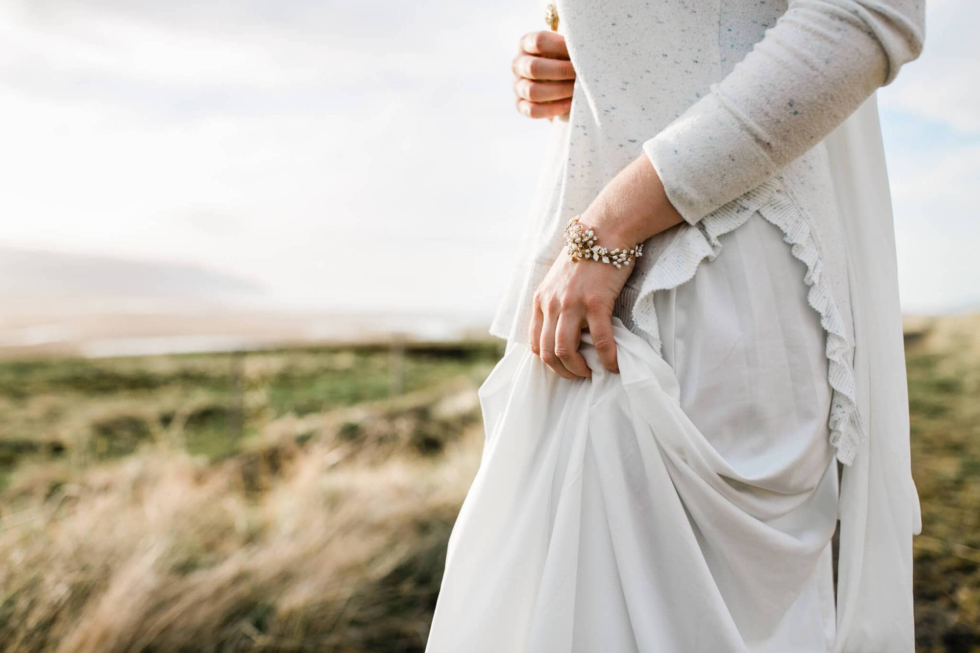 A detail picture of a bride holding her skirt in a field during her Iceland Elopement.