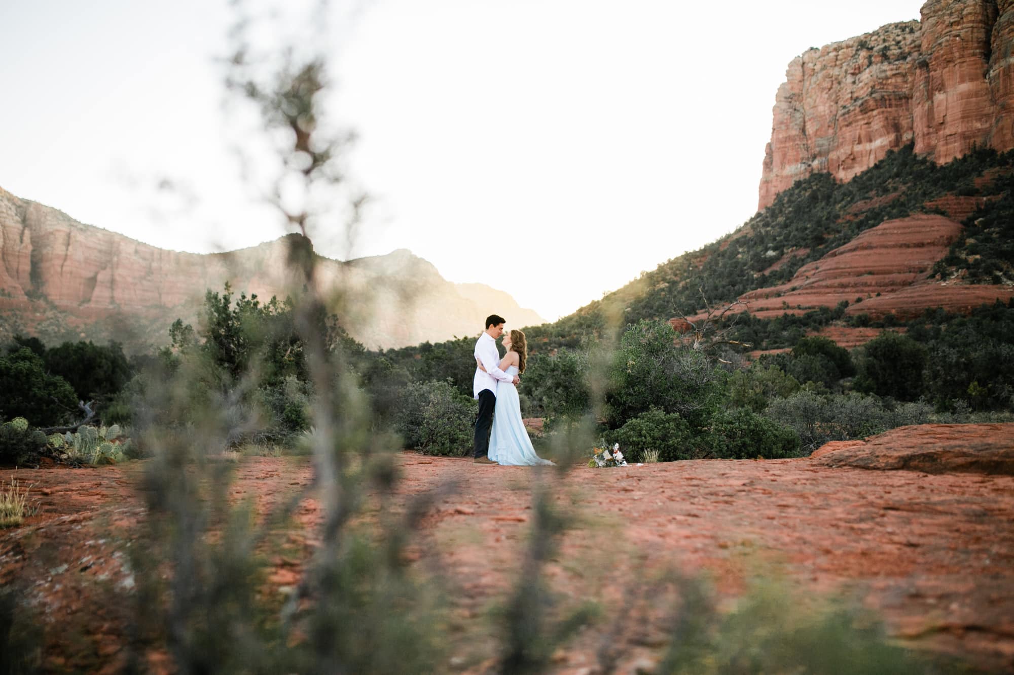 Framed by desert scrub with the sun rising behind them, the couple looks at each other during their Sedona Adventure Wedding.