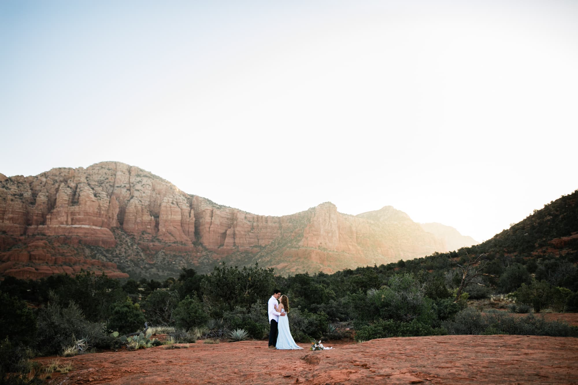 The couple appear tiny as the sun rises over the red Sedona mountains.