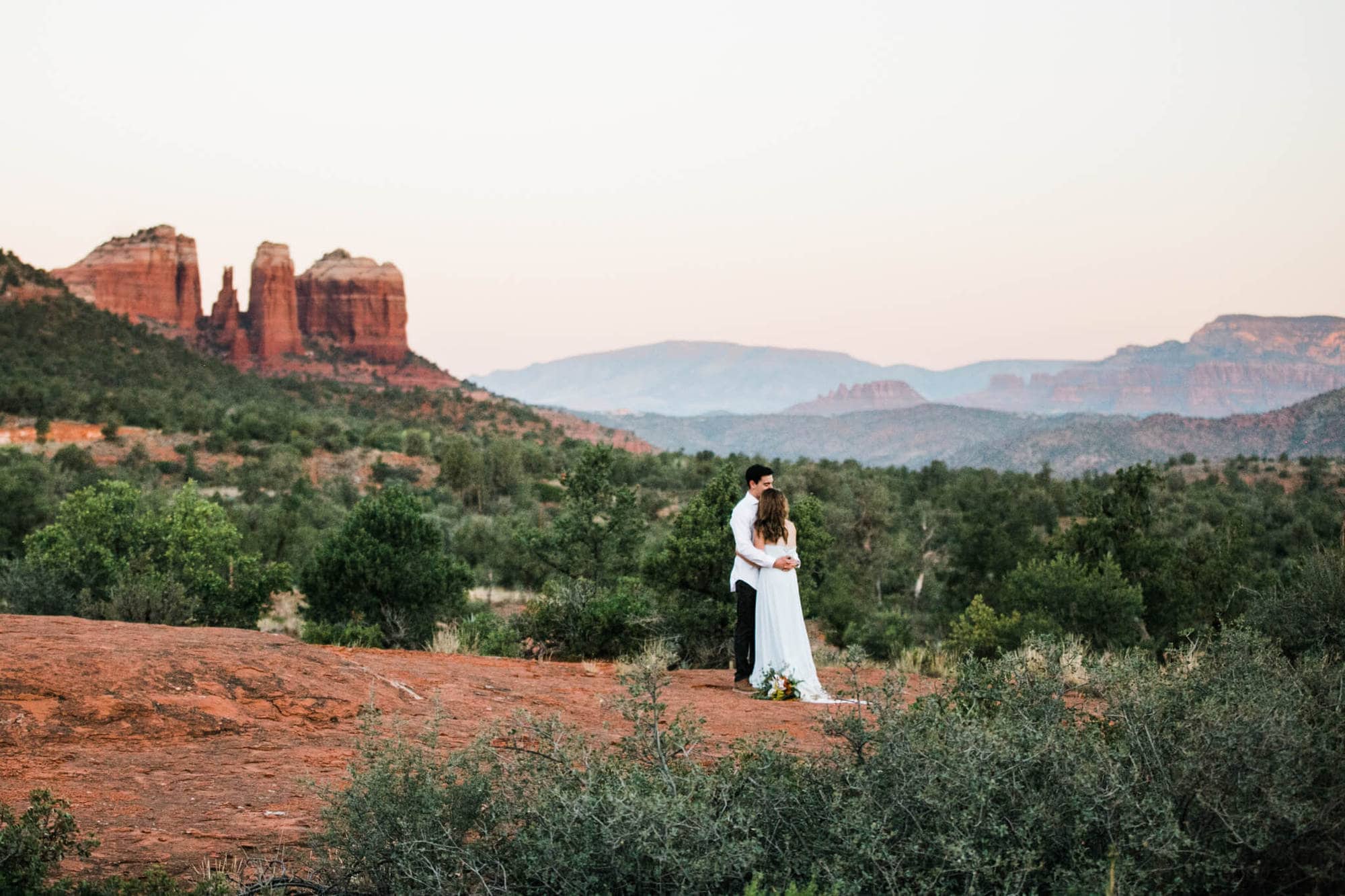 With Cathedral Rock behind them, the bride and groom look out over Sedona as the sun starts to rise.