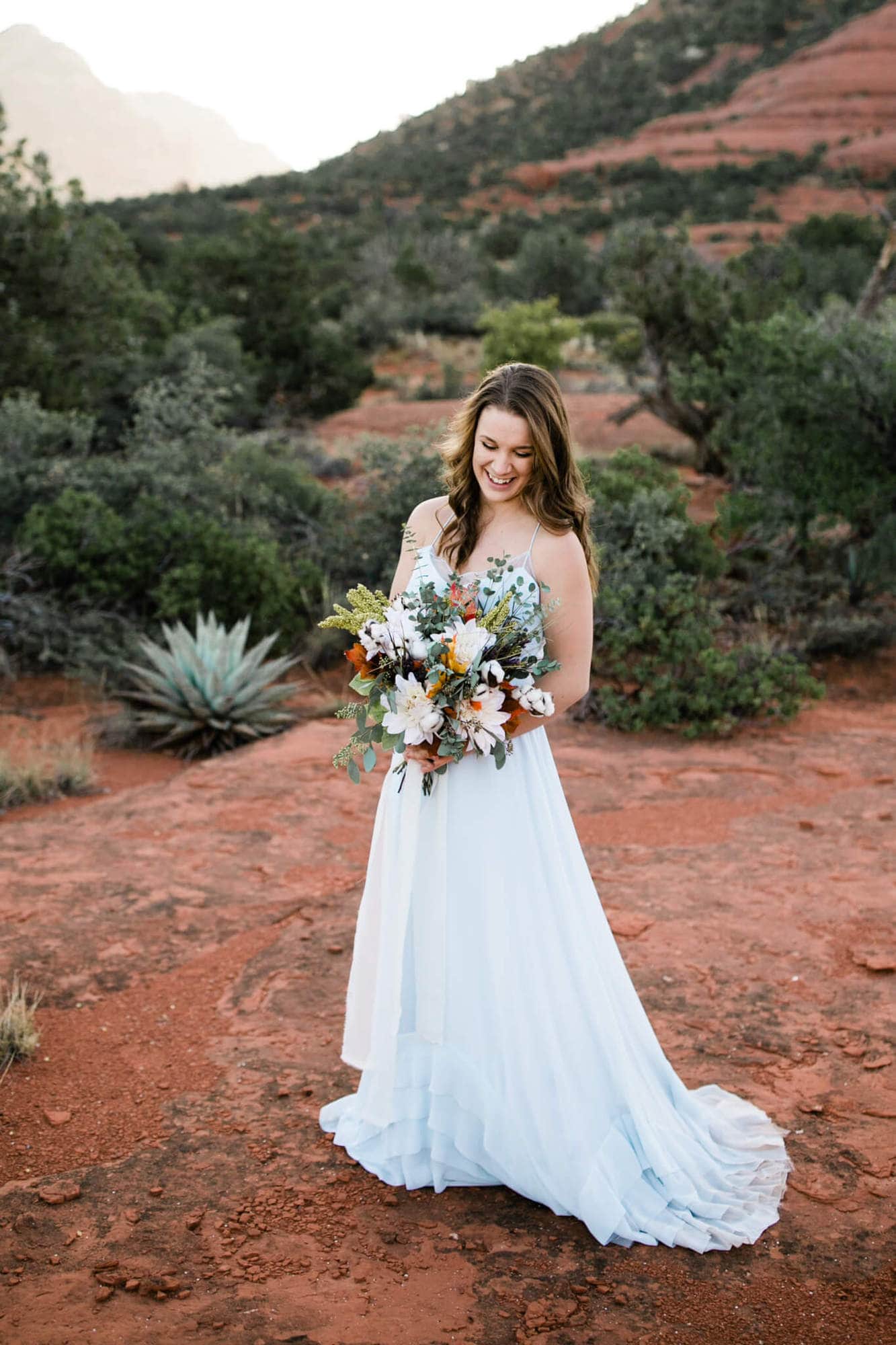 The bride poses for a bridal portrait, holding her bouquet and laughing.