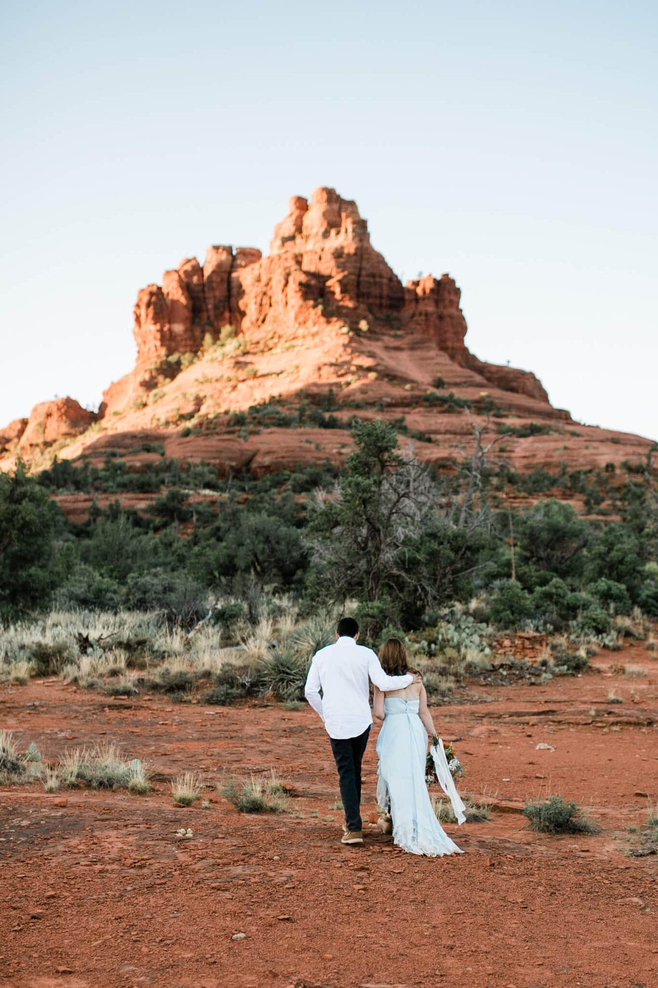 With his arms around her shoulders, the groom and bride walk towards Bell Rock.