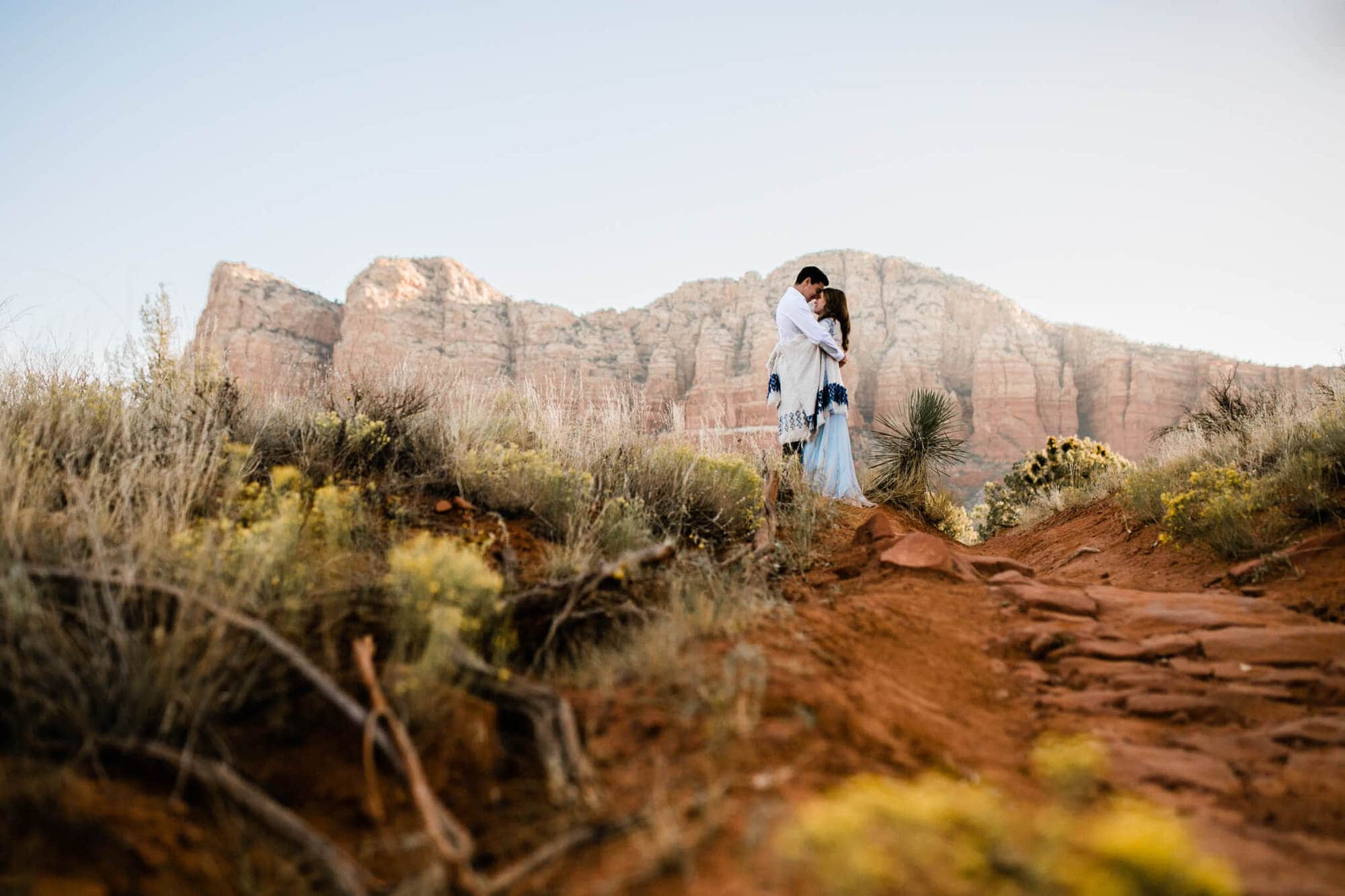 Framed by the epic red mountains behind them, the bride and groom hug in a field of yellow flowers during their Sedona Adventure Wedding