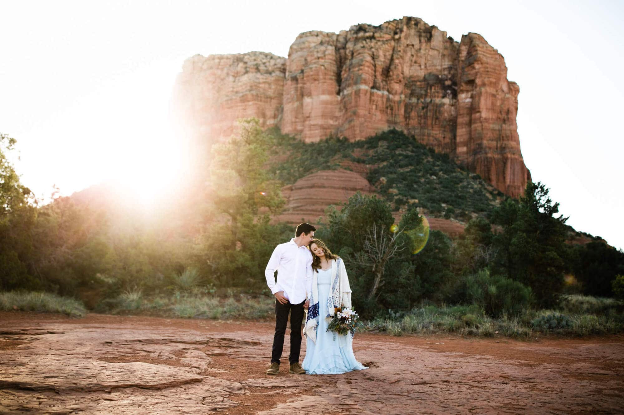 The bride rests her head on her groom's shoulder. He kisses her head and Courthouse Butte stands tall behind them.
