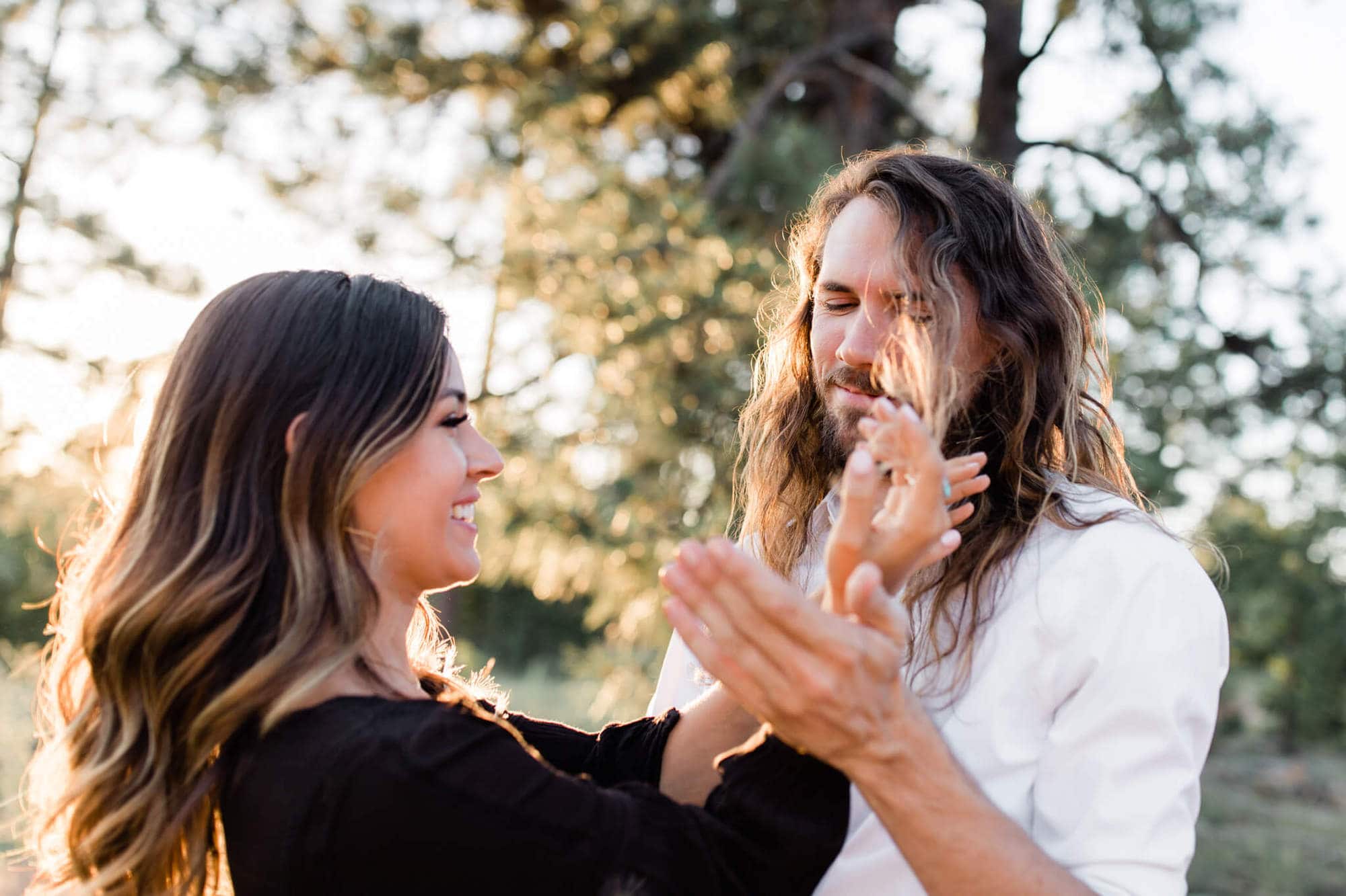 Laughing, Leah picks Dandelion fluff out of David's hair during their forest engagement photo session.
