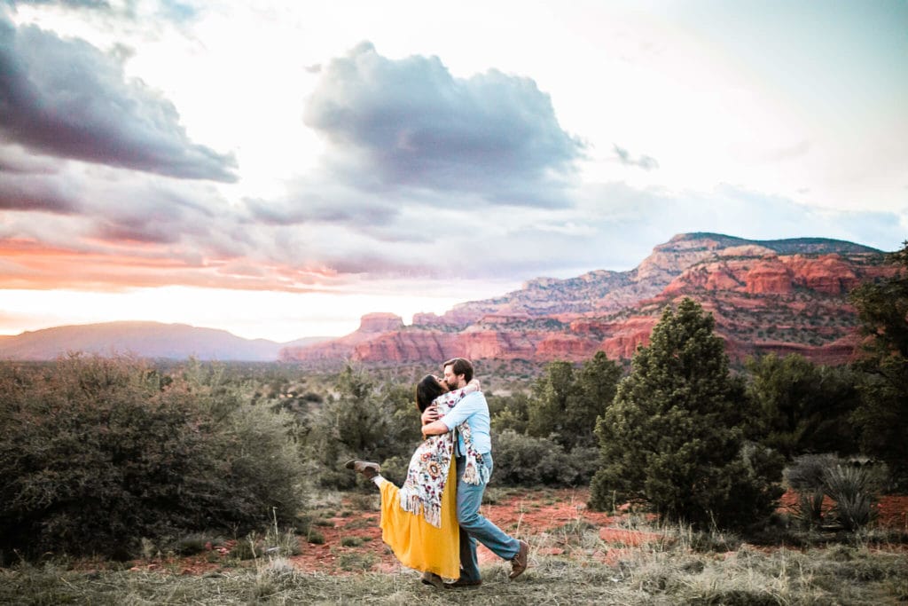 The bride and groom kiss during their elopement. The red rocks of Sedona glow in the sunset behind them.