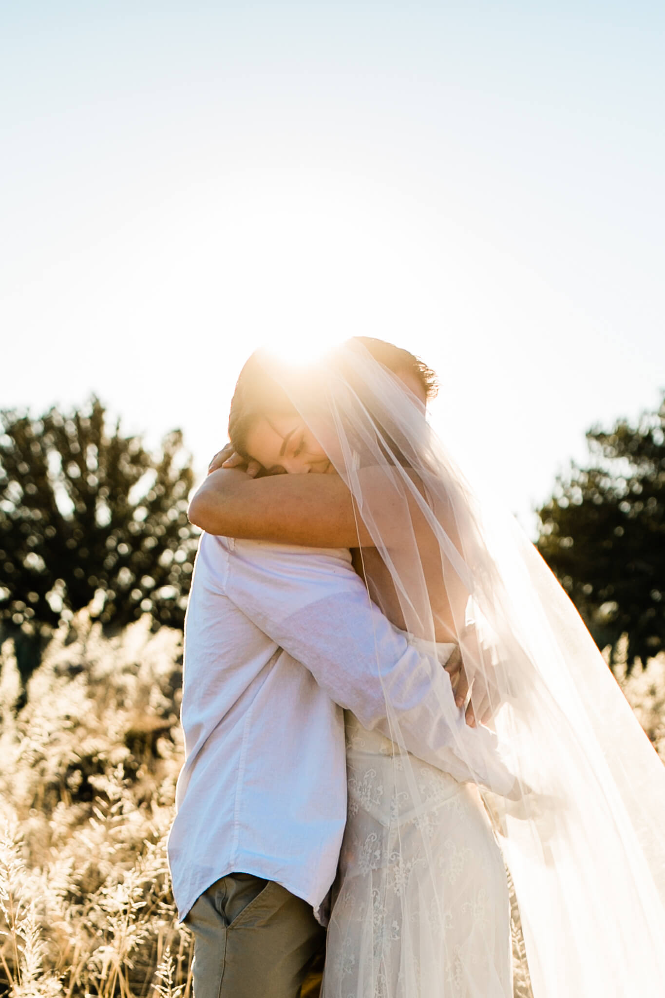 The bride hugs the groom with the sun bursting behind them.