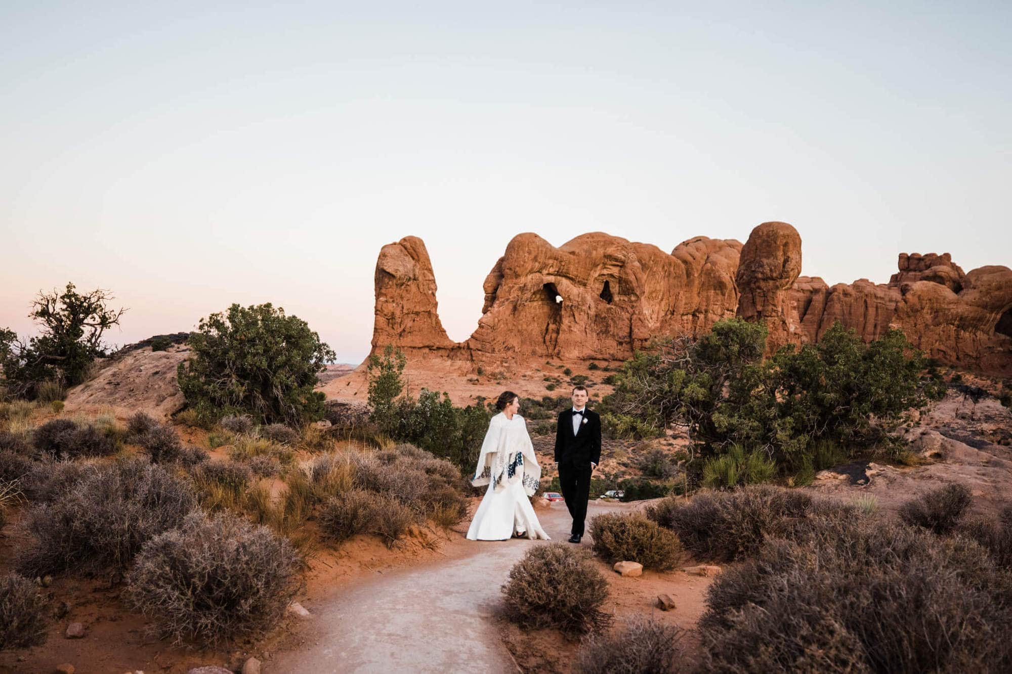 Bride and groom walk at sunrise for their Arches National Park wedding.