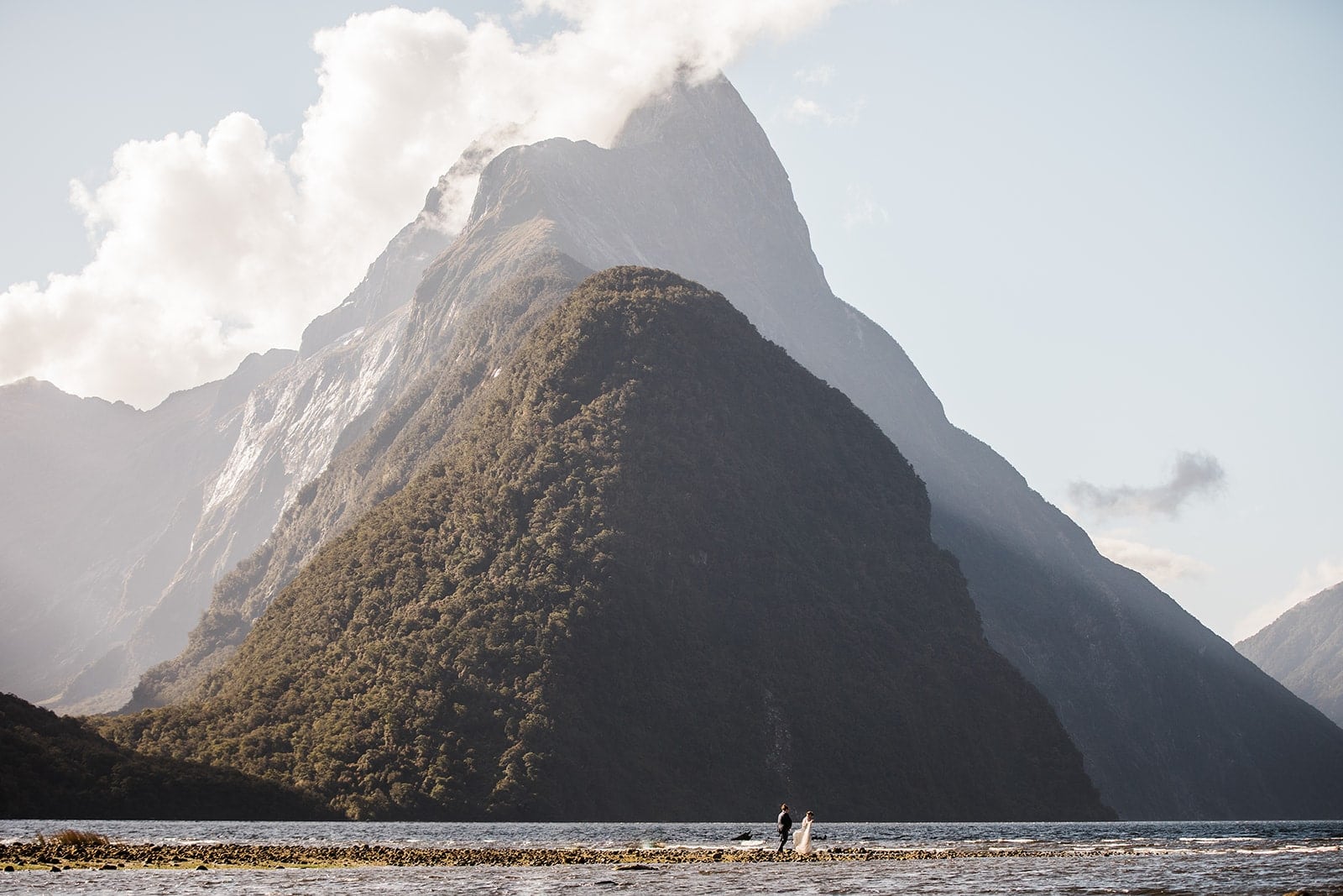 Bride and groom hold hands while walking around Milford Sound during their New Zealand elopement