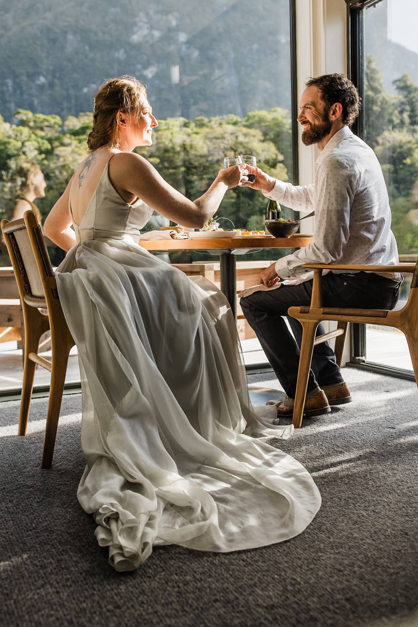 A bride and groom toast over their meal in Milford Sound Lodge during their New Zealand elopement.
