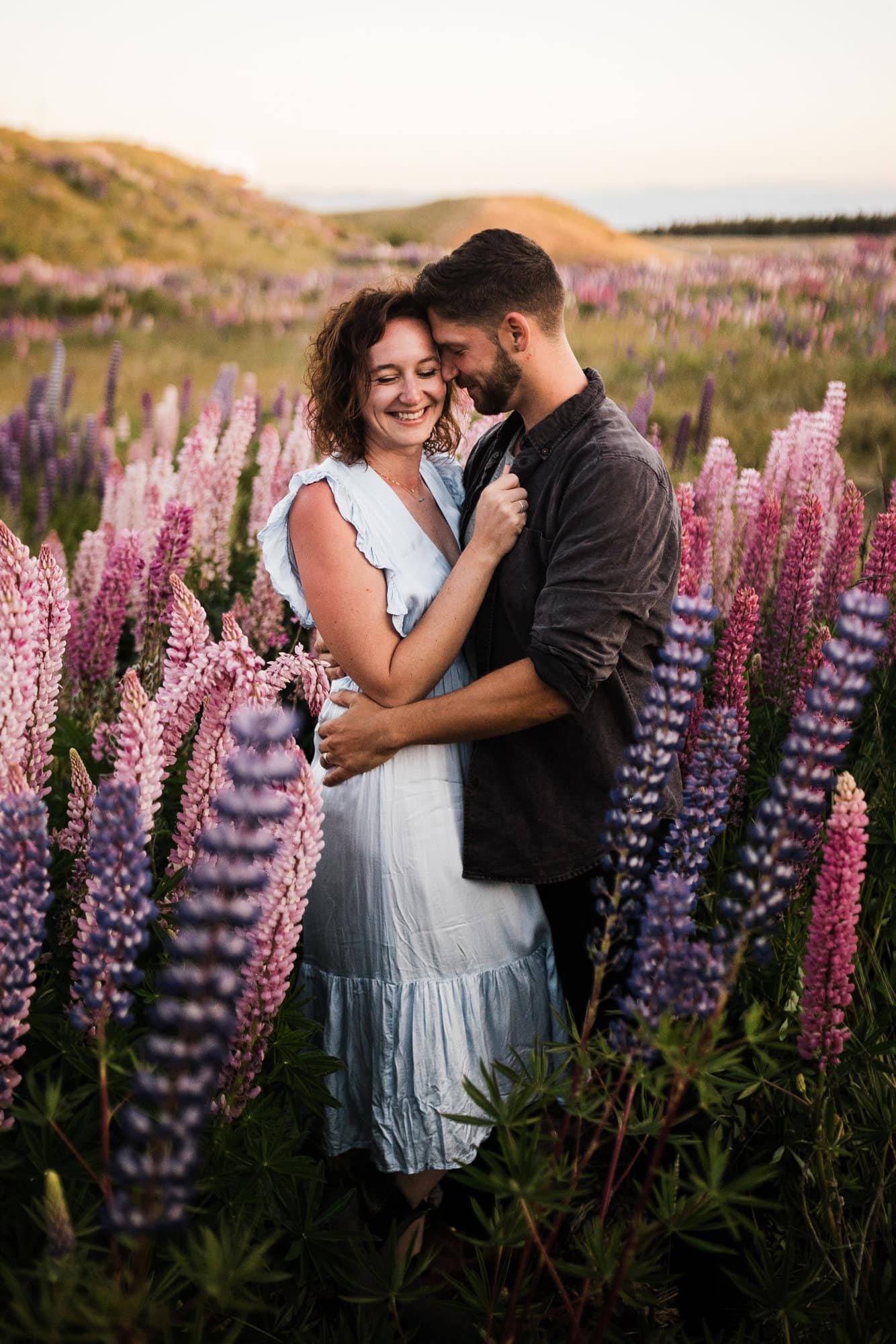 A couple hug in a field of lupines while getting New Zealand elopement photos