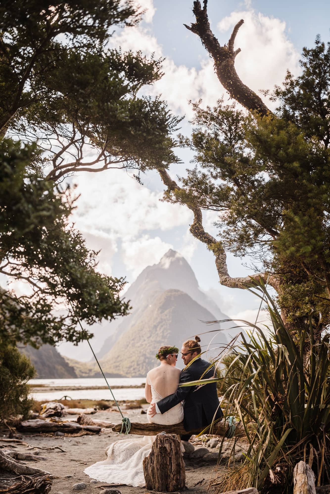 Bride and groom sit on a wood swing overlooking Milford Sound during their elopement in New Zealand