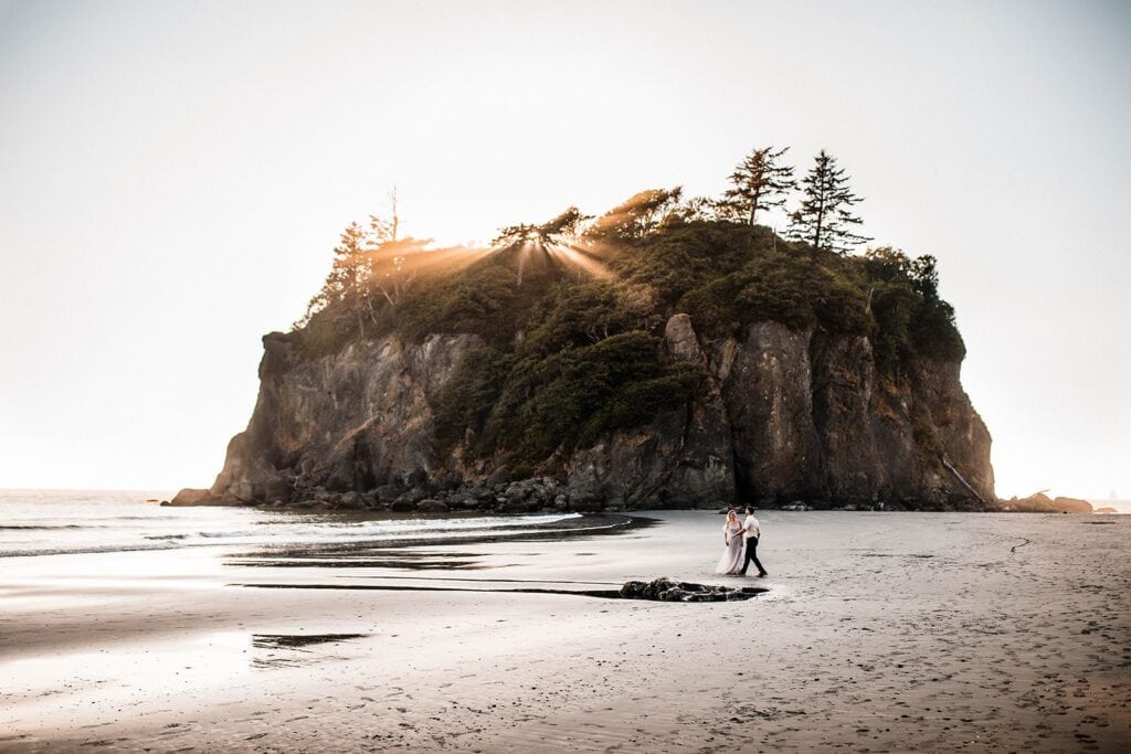 Bride and groom hold hands while walking across the beach during their elopement in Olympic National Park