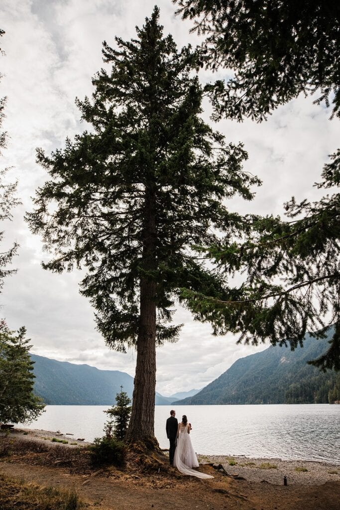 Bride and groom hold hands while standing beside the lake during their elopement in Olympic National Park