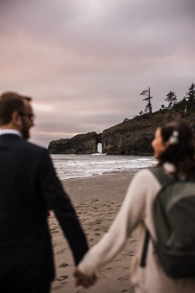 Bride and groom hold hands as they walk across Second Beach during their Olympic National Park elopement