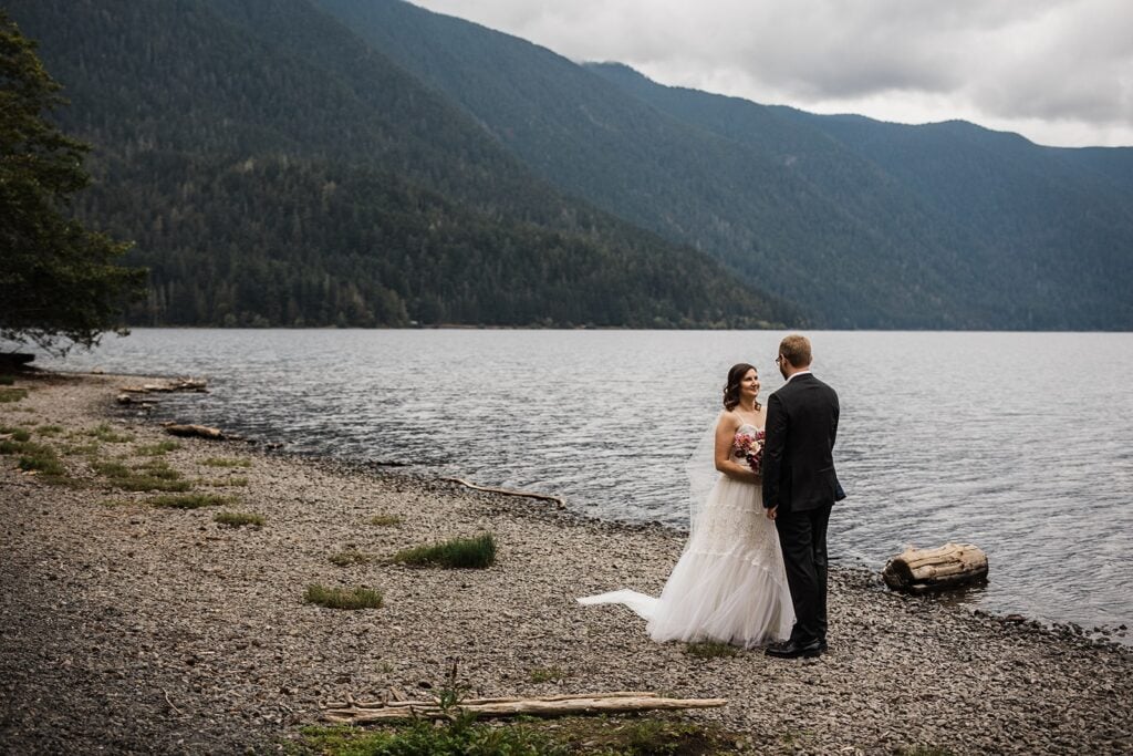 Bride and groom hold hands while standing by Lake Crescent