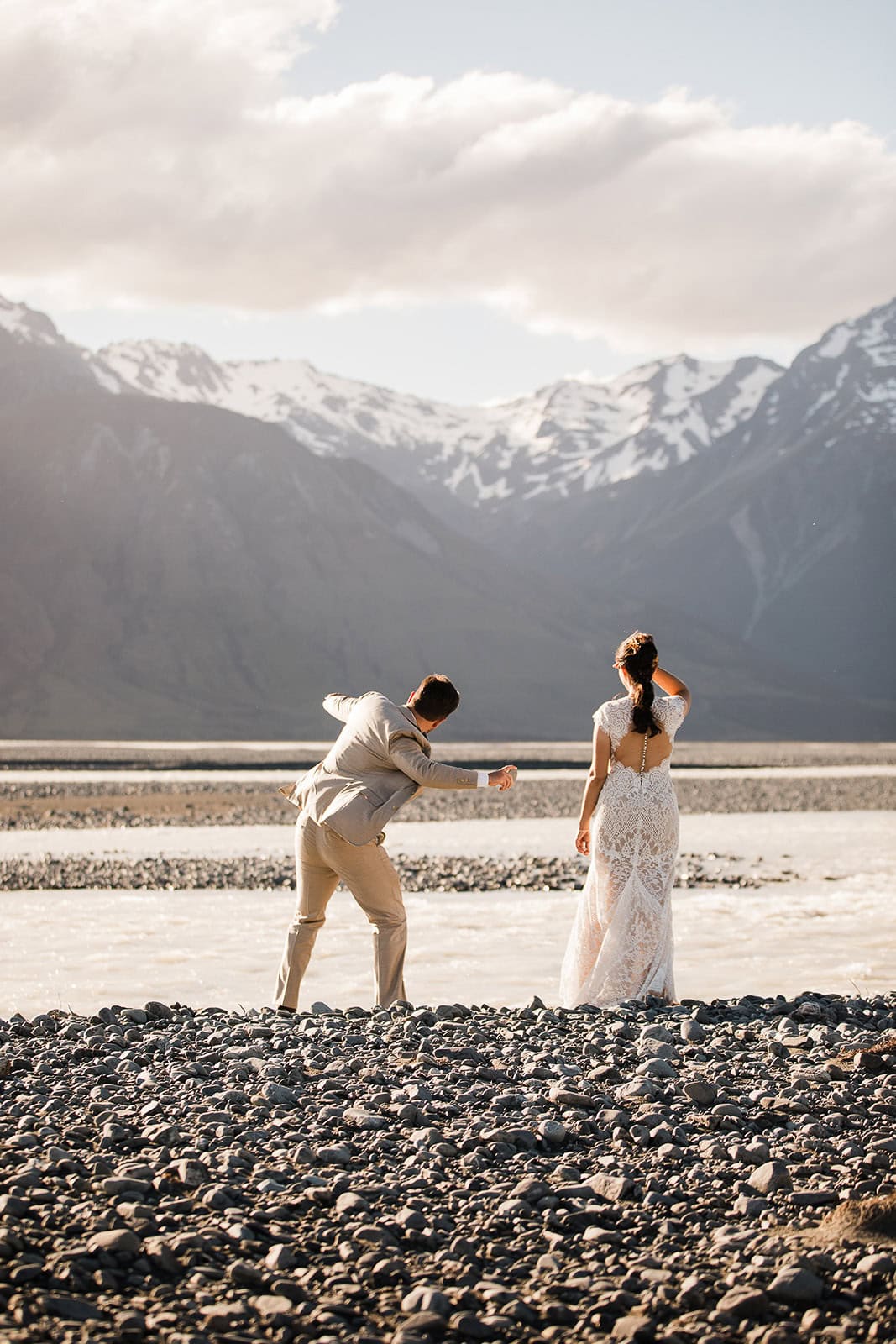 newlyweds skipping stones with mountains in the background while in New Zealand, one of the best winter elopement destinations.