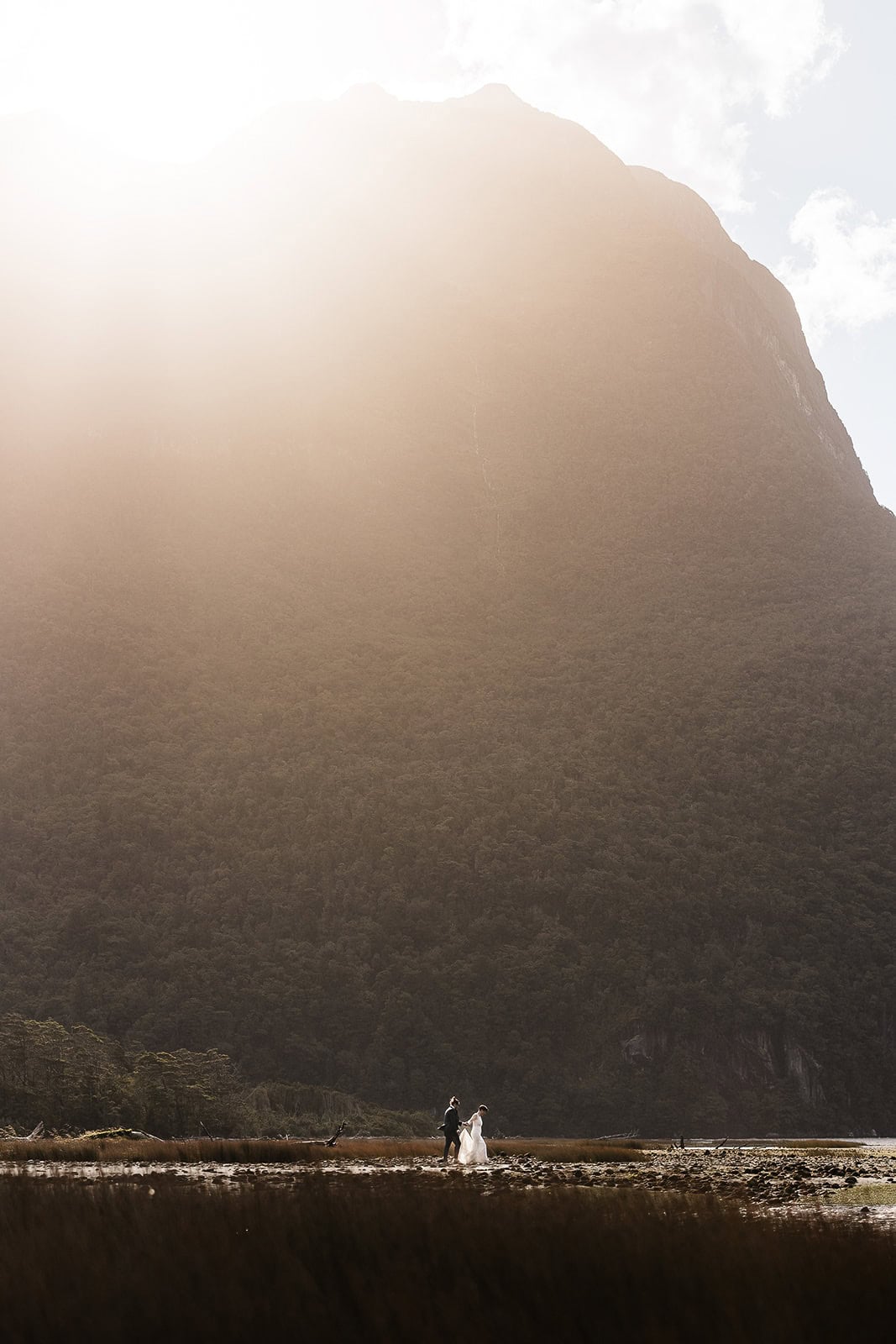 newlyweds walking on the beach with a large mountain behind them in New Zealand.