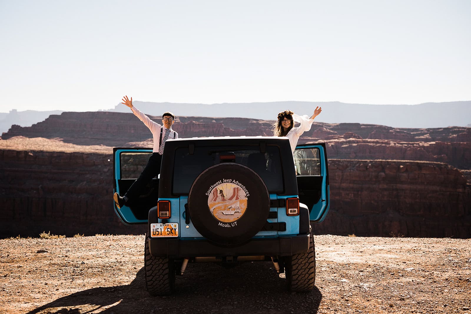 newlyweds waving from a jeep in the desert, showcasing what an elopement can look like.