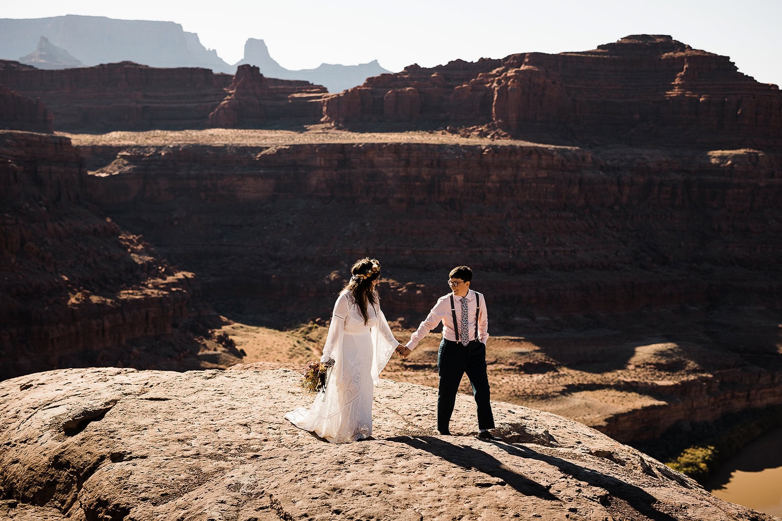newlyweds holding hands in the desert by a canyon.