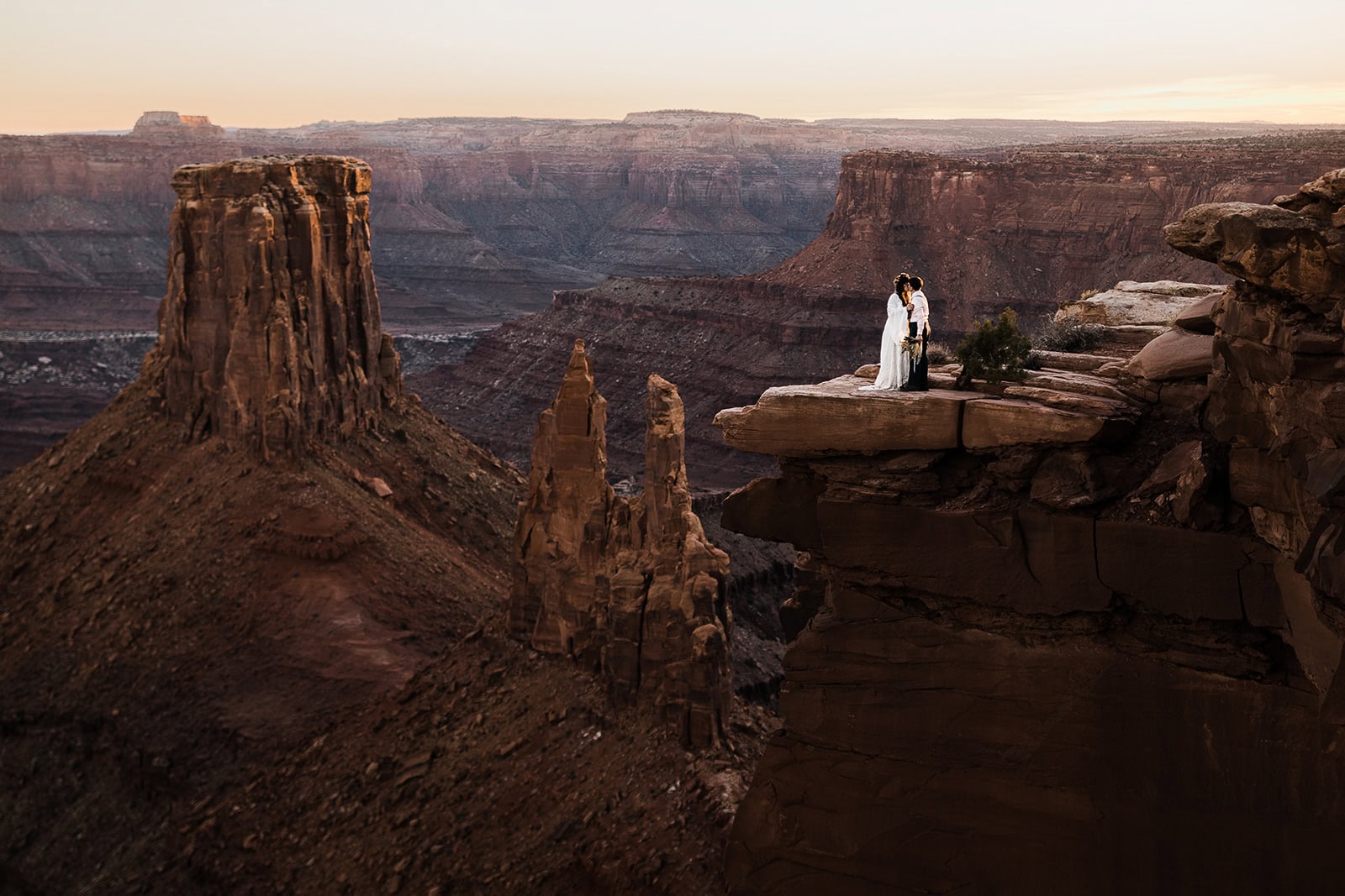 newlyweds standing at the edge of a canyon at sunset, kissing. 
