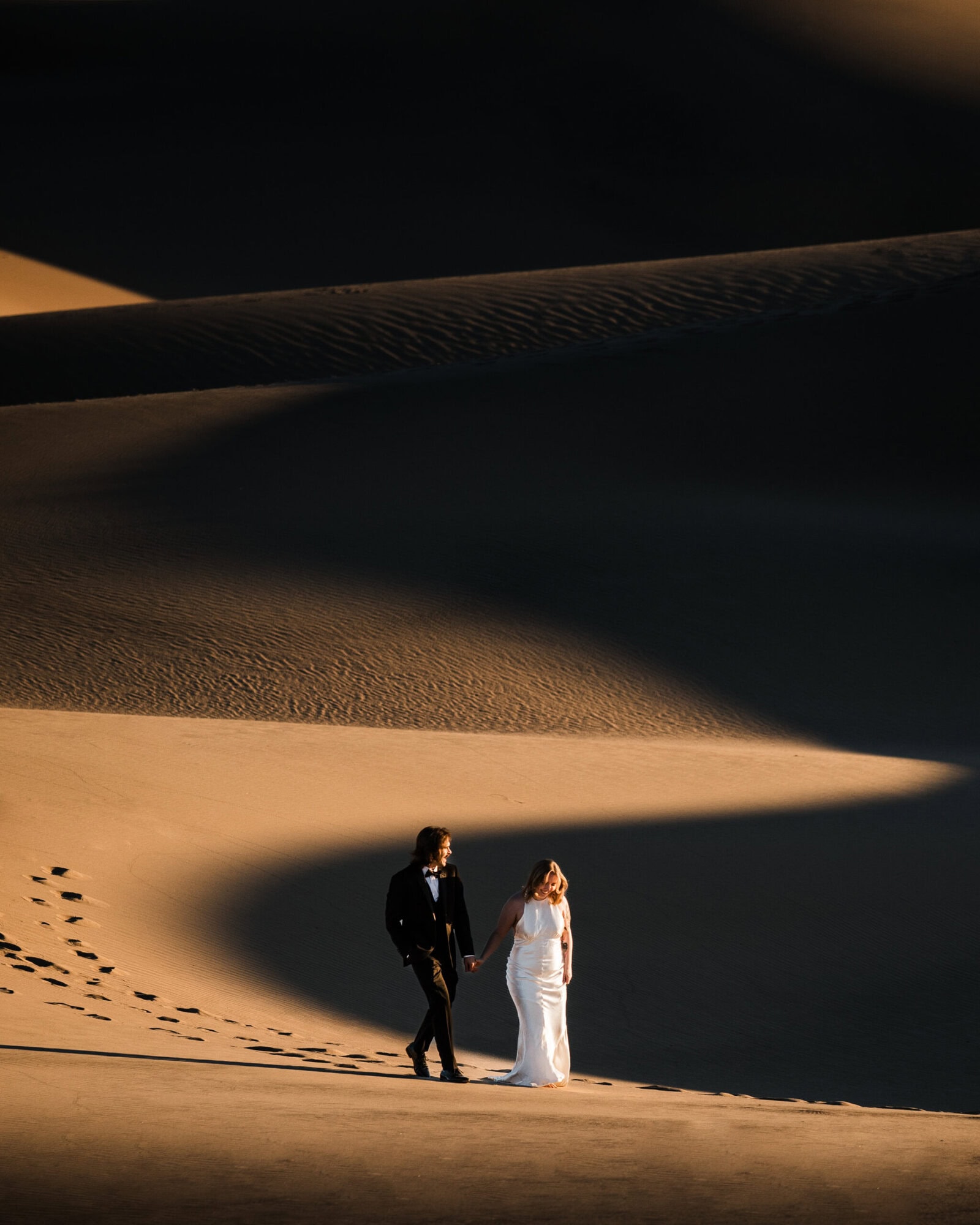 A bride and groom walk in the shadow of a sand dune in Death Valley on their elopement day