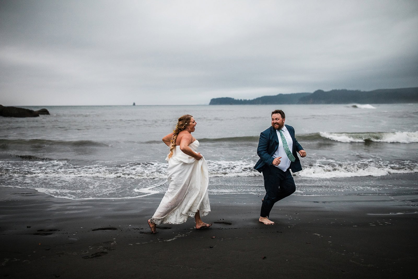 newlyweds running on a black sand beach in olympic national park.