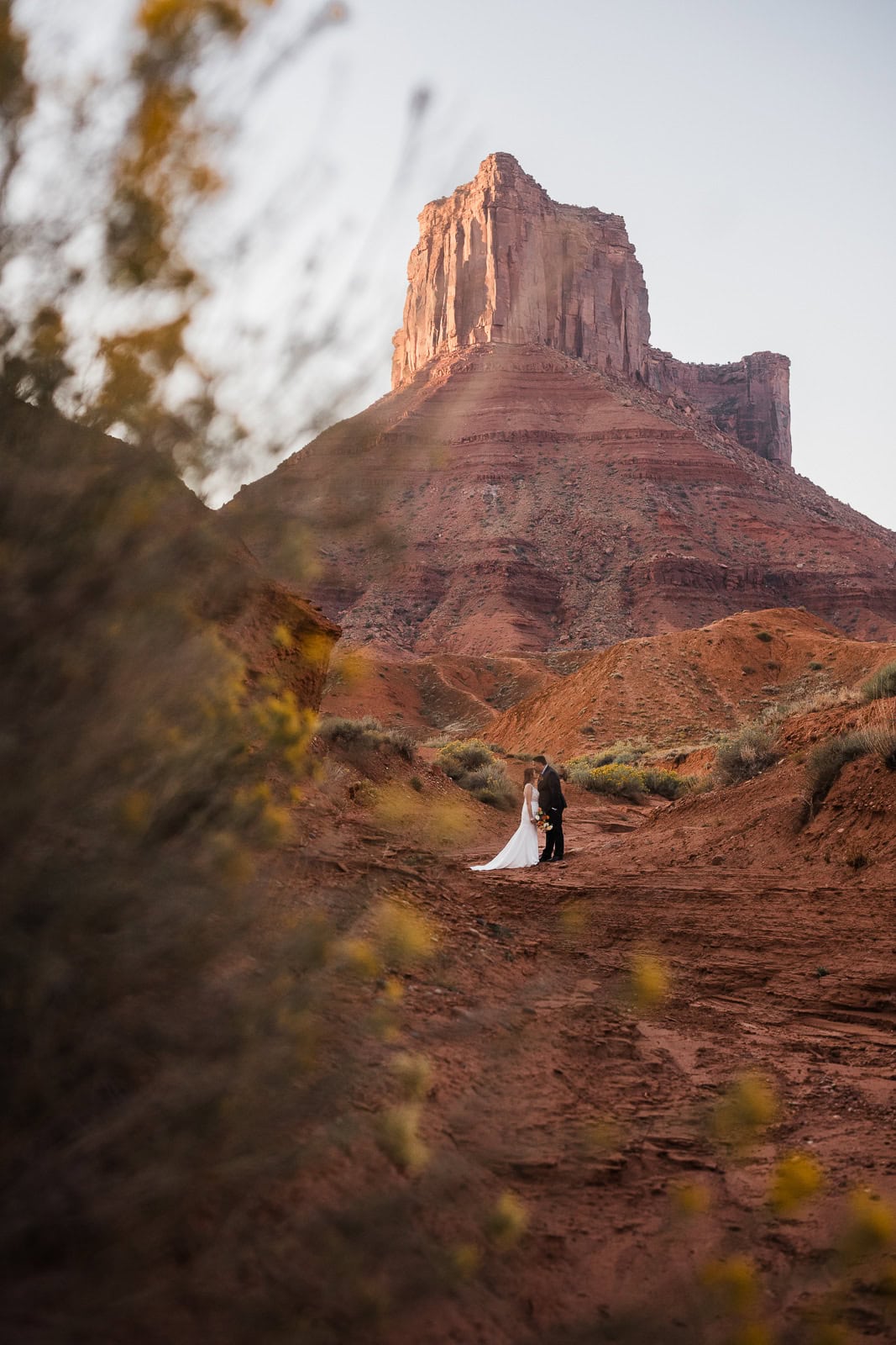 newlyweds hugging in front of a large sandstone tower.