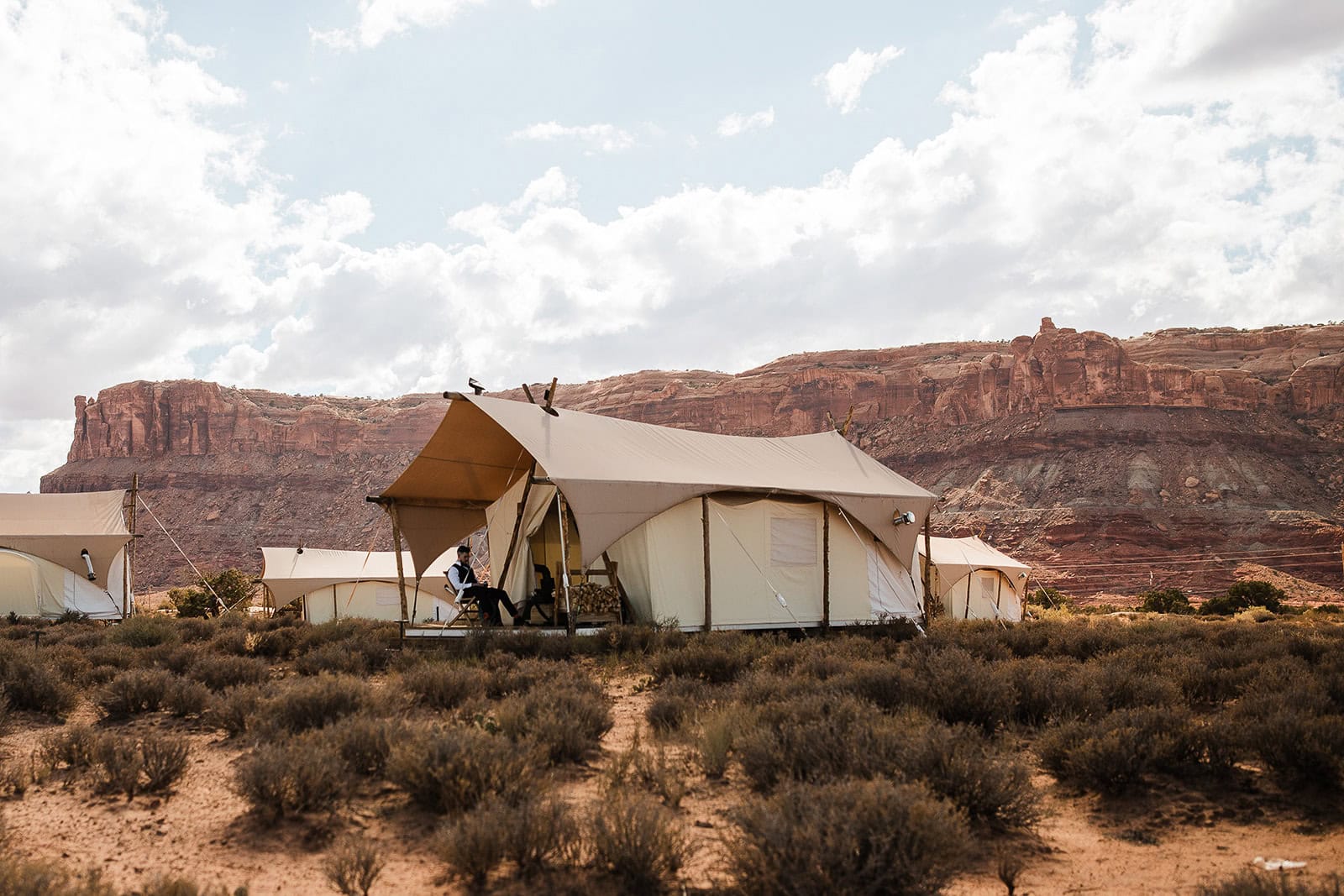 Under Canvas canvas tent with the groom and bride sitting outside.
