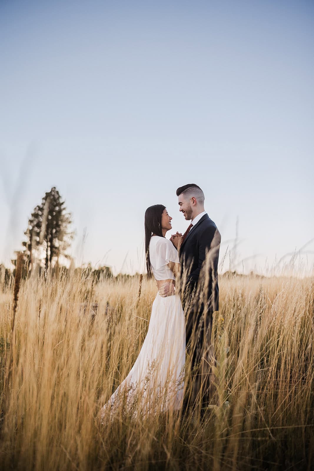 newlyweds standing in a field at sunrise.