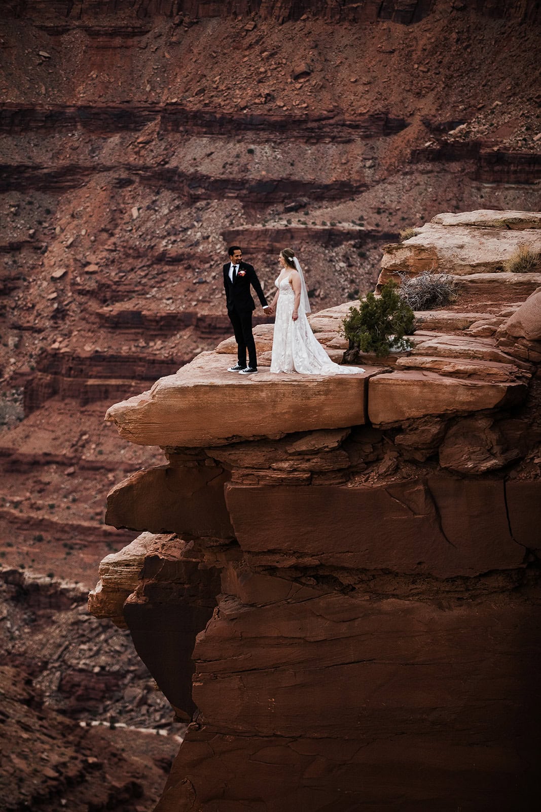 newlyweds holding hands at the edge of a canyon in moab.
