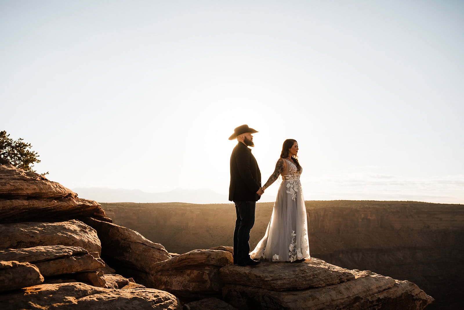 Newlyweds holding hands at the edge of a canyon in fall, one of the best seasons to consider when deciding when to elope in Moab.