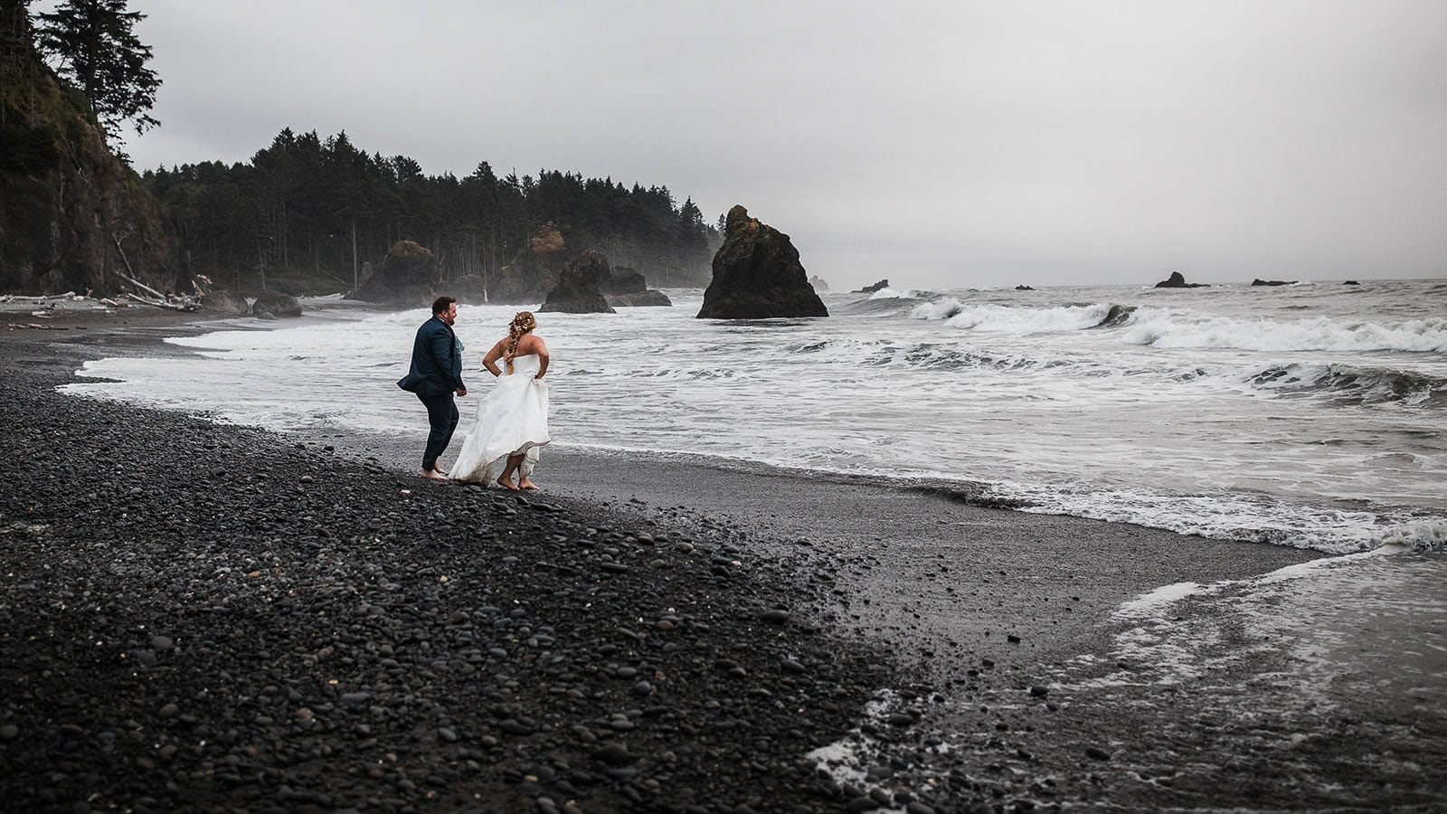 newlyweds running into the ocean along the pacific coast.