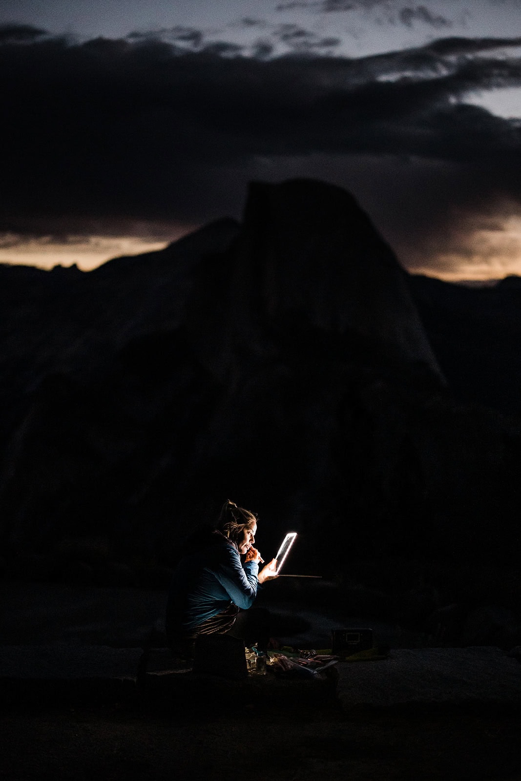 the bride adjusting makeup in front of half dome before sunrise, saving money on the cost to elope.
