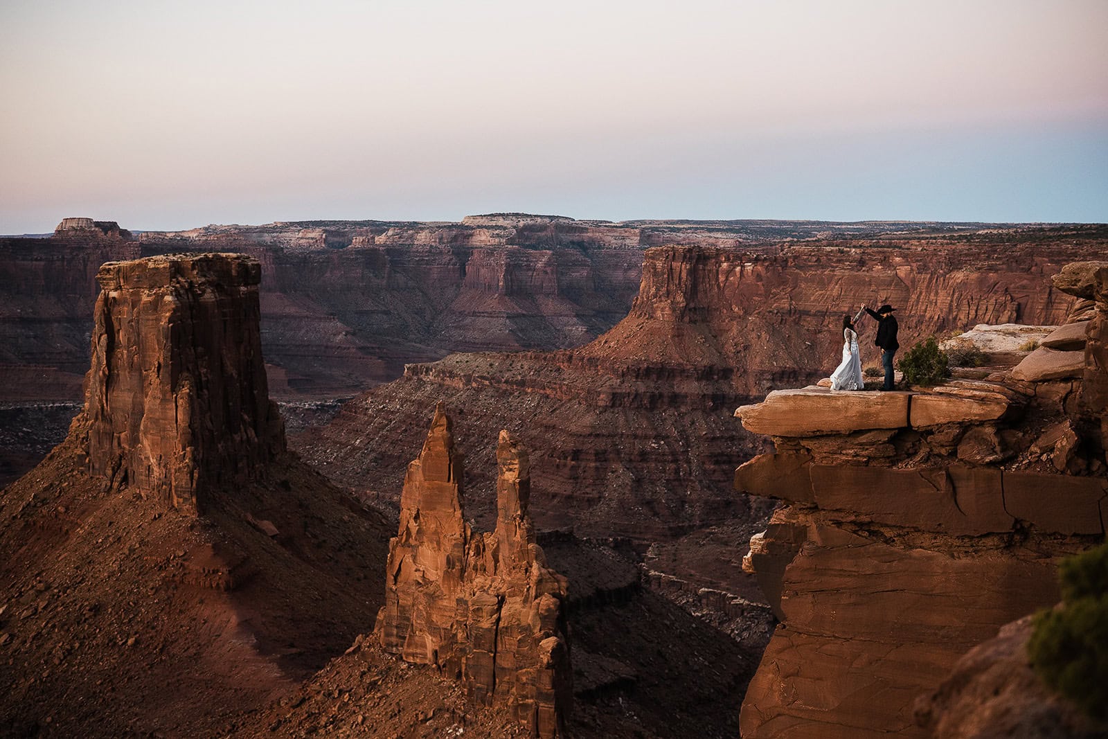 Newlyweds dancing at the edge of a canyon in Moab as part of their wedding in the La Sal Mountains.