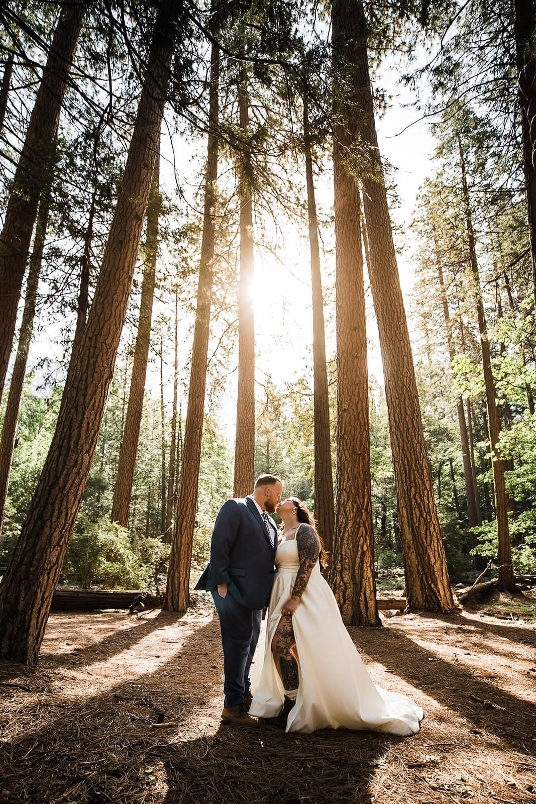 Newlyweds kissing in a grove of pine trees.