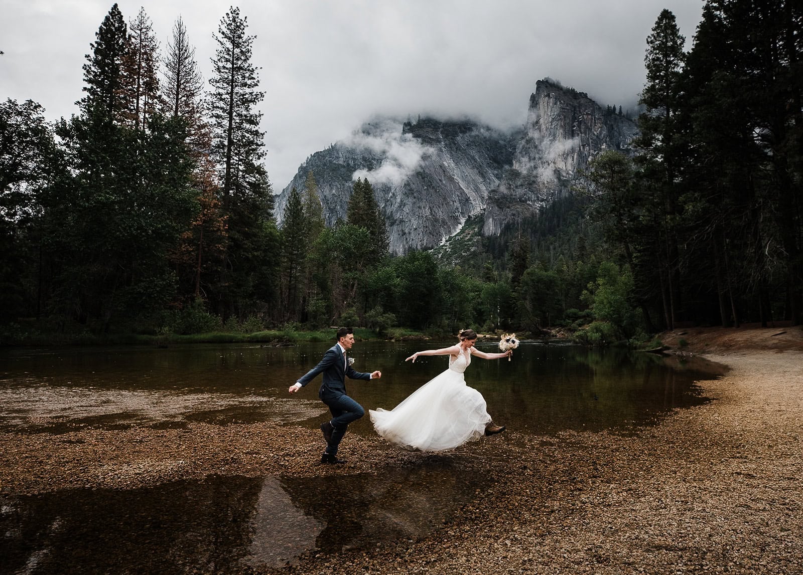 Newlyweds jumping over a stream in Yosemite valley, one of the best Yosemite wedding locations.