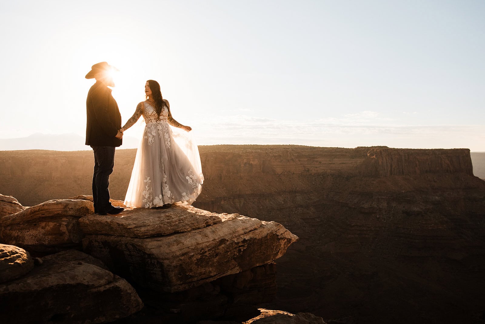 Newlyweds holding hands at the edge of a canyon in Moab during their wedding in the La Sal Mountains.