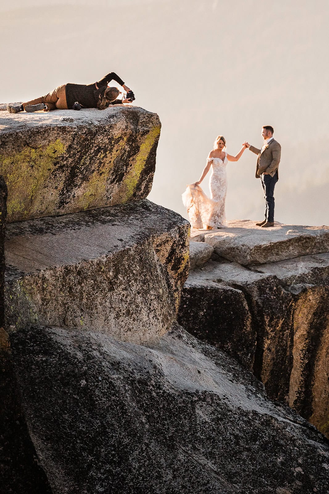 newlyweds holding hands while a photographer lays on her side to capture them.